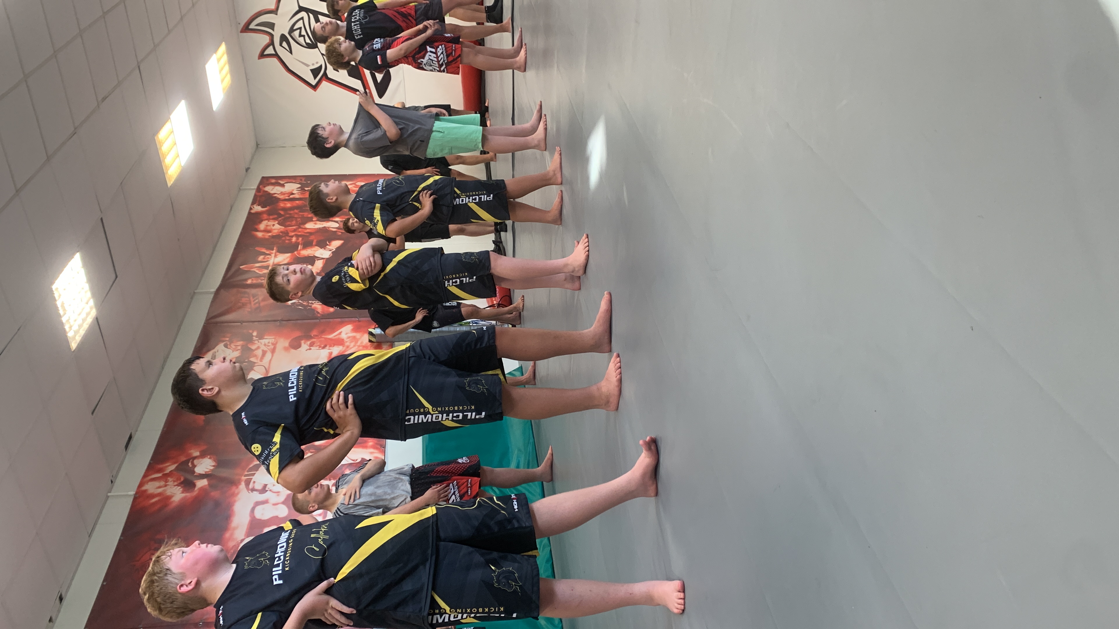 Uczniowie Kickboxing Pilchowice w czarno-żółtych strojach stoją w równym szeregu przed rozpoczęciem egzaminu