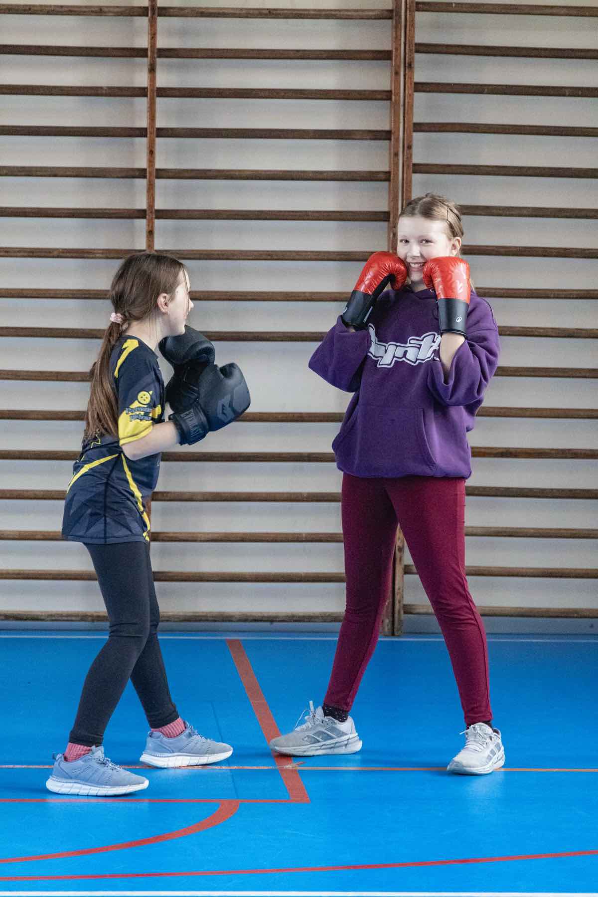 Dwie dziewczynki podczas sparingu, jedna uśmiechnięta w czerwonych rękawicach